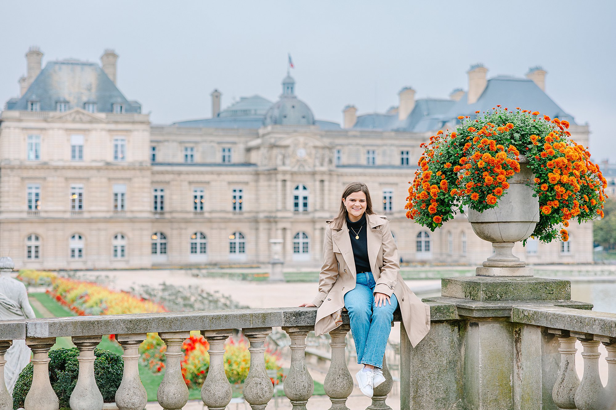 A woman sits on the balustrade near flowers in Luxembourg Gardens during a relaxed Paris photoshoot