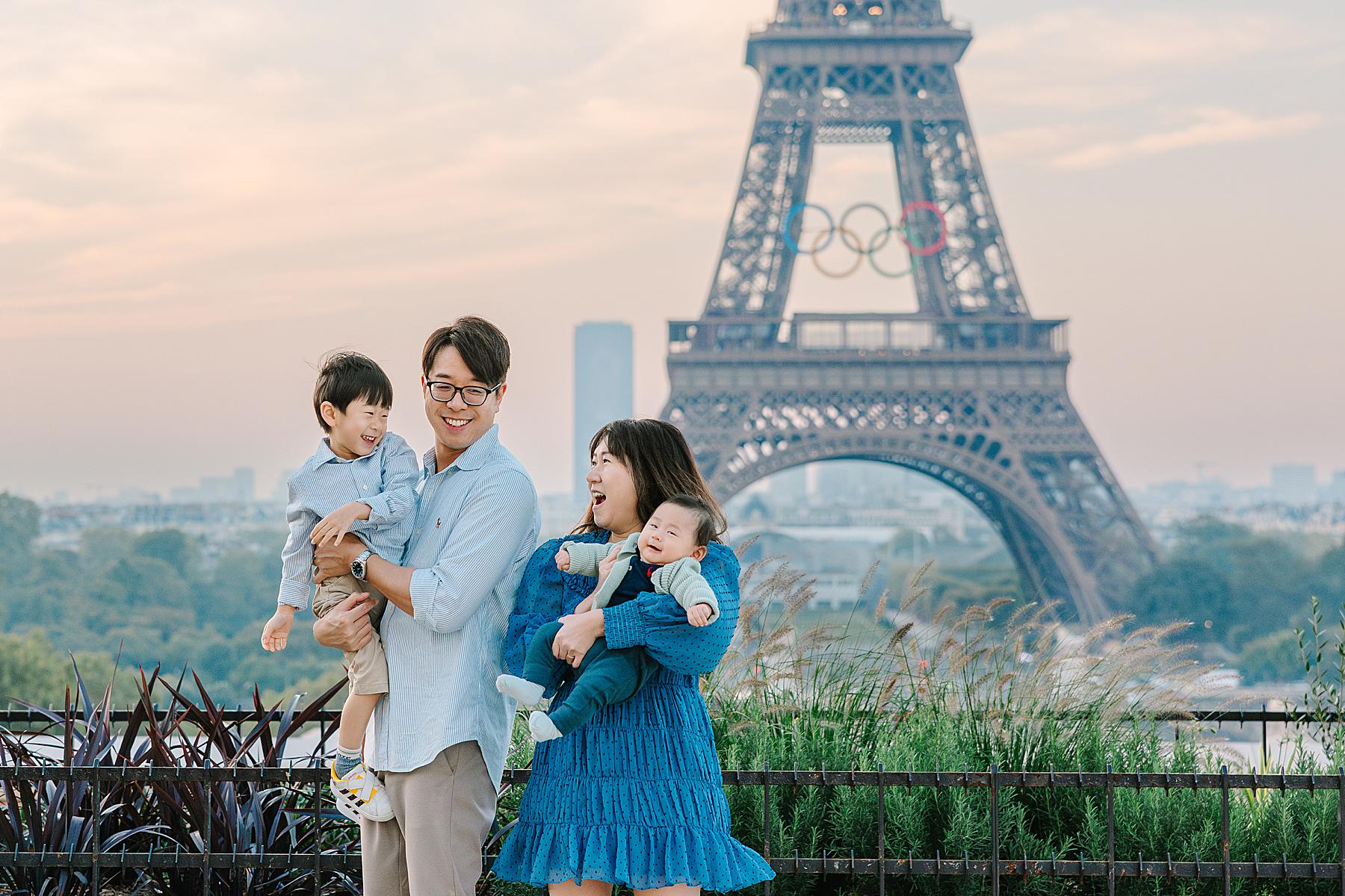 A family of four dressed in coordinated blue outfits poses playfully in front of the Eiffel Tower at sunrise during their Paris photoshoot
