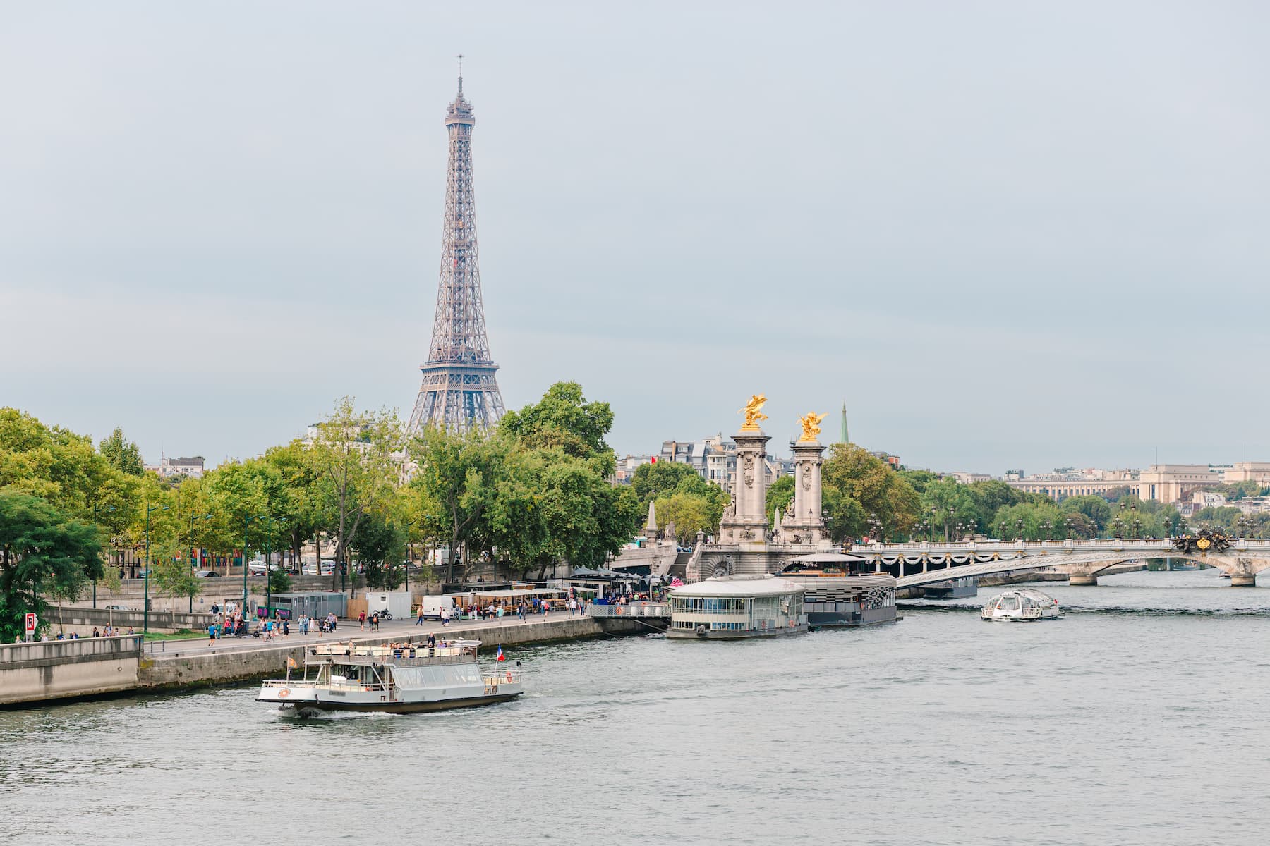 View of the Eiffel Tower and the Seine River with spring greenery and boats passing beneath the Pont Alexandre III bridge in Paris, May 2025